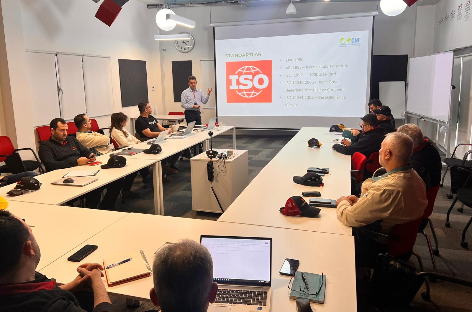 Bir üretim tesisinin eğitim salonunda kurum içi yaşam döngüsü analizi eğitimi; ekranda ISO 14040 ve ISO 14044 standartları slaydı